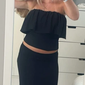 Svart bandeau tubtopp med volang - Säljer en svart bandeau tubtopp med volangdetalj upptill. Toppen är axelbandslös och sitter tight runt kroppen.