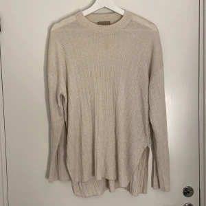 Beige ribbad stickad tröja H&M XS - Beige ribbstickad tröja från H&M i storlek XS. Tröjan har lång ärm, rund halsringning och slitsar i sidorna för en chill och avslappnad vibe. Perfekt för lager-på-lager under hösten och vintern. Har en fundaction fläck på därav billigt pris.