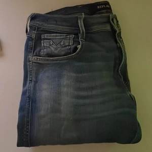 Replay Anbass blå jeans slim fit - Säljer ett par Replay Anbass jeans i snyggt tvättad blå färg med klassiska fem fickor och slim fit passform. Jeansen har låg midja och raka ben, tillverkade i stretchig bomull för skön komfort. Perfekt för dig som gillar stilrena och moderna jeans.