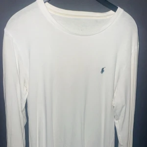 Vit långärmad tröja från Polo Ralph Lauren - Vit långärmad tröja från Polo Ralph Lauren med klassisk rund hals och den ikoniska lilla loggan broderad på bröstet. Mjuk och skön bomull som passar perfekt till jeans eller shorts. Enkel och stilren design för en clean look.