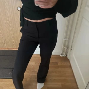 Svarta kostymbyxor med raka ben - Snygga svarta kostymbyxor med raka ben och midjehällor. Byxorna har klassisk passform och stängs med dragkedja och knapp. Perfekta för en clean och stilren look. Materialet känns mjukt och följsamt.