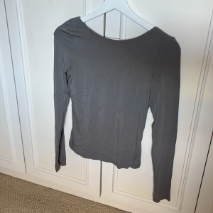 Grå långärmad topp med öppen rygg - En basic grå långärmad topp från Bik Bok i mjuk bomull. Superfin detalj med öppen rygg baktill, knappt använd!
