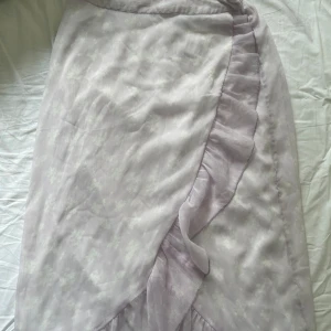 Ljuslila omlottkjol  - Supersöt ljuslila omlottkjol från Vero Moda med volangkant och diskret blommigt mönster. Kjolen är aldrig använd och därför jag säljer den ☺️