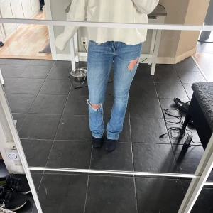 Ljusblå slitna bootcut jeans - Säljer ett par ljusblå jeans med slitningar på knä och lår. Modellen har låg midja och bootcut-ben, vilket ger en snygg siluett. Jeansen är i klassisk denim och har fem fickor samt dragkedja och knapp framtill. Från Zara. Midjemått 38 cm rakt över, innerbenslängd 80cm.
