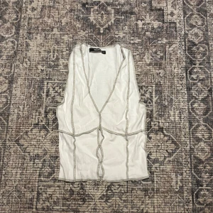 Vit ribbad linnetopp från Bikbok - Säljer en vit ribbad linnetopp från Bikbok i storlek XS. Toppen har markerade sömmar i kontrastfärg och en djup v-ringning framtill. Den är ärmlös och har en figurnära passform, perfekt för att styla med jeans eller kjol.