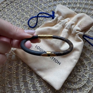 Louis Vuitton armband i monogram - Snyggt armband från Louis Vuitton med klassiskt monogrammönster i brunt och svart läder. Detaljer i guldmetall och stilren, rund form. Perfekt accessoar för dig som gillar lyxiga och tidlösa smycken. Kommer med original dustbag och kvitto. Aldrig använt.  Ordinariepris 3200 kr. Storlek: 17 