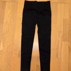 Svarta scrunch leggings i polyamid - Svarta leggings med scrunch-detalj bak som framhäver formen. Hög midja och tight passform, perfekta för gymmet eller chill hemma. Materialet är stretchigt med 90% polyamid och 10% elastan för maximal komfort och rörelsefrihet.