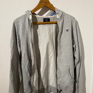 Hackett grå hoodie - Säljer en stilren grå hoodie från Hackett London med huva och dragkedja framtill. Barnstorlek, sitter som en XS