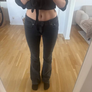 Svarta bootcut jeans med låg midja - Säljer ett par svarta jeans med bootcut-modell och låg midja. Jeansen har klassisk femficksdesign och är i ett mjukt denimtyg som sitter snyggt över höfterna och låren innan de släpper ut vid bensluten. Perfekta för dig som gillar en retro vibe.