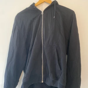 Svart hoodie med dragkedja från Weekday - Chill hoodie från Weekday i bomull med hel dragkedja framtill, huva med snörning och två stora fickor. Perfekt för en chill och avslappnad stil. Långärmad och i klassisk passform.