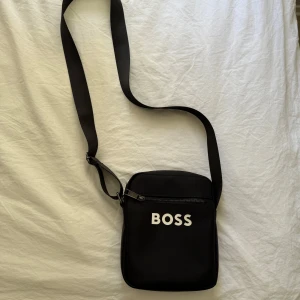 Svart Axelväska  - Snygg och praktisk axelremsväska i bra skick. 	•	En större huvudficka med 2 extra innerfack (en med dragkedja) för organisering. 	•	En framficka för mobilen eller småsaker 	•	Justerbar axelrem  Perfekt för vardag, skola eller resor.