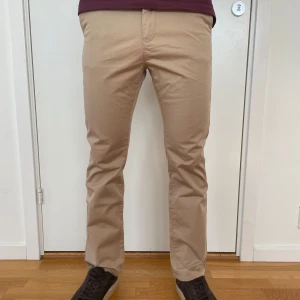Beige chinos från Gant - Aldrig använda snygga beige chinos från Gant med klassisk rak passform och midwaist. Byxorna har fickor fram och bak, bälteshällor och stängs med knapp och dragkedja. Tillverkade i mjuk bomull som är skön att ha på sig. Perfekta för en clean och stilren outfit. Tveka inte att kontakta för frågor.