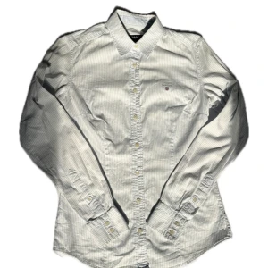 Vitblå randig skjorta från GANT - Klassisk skjorta från GANT i vit och ljusblå randigt mönster. Skjortan har lång ärm, knappar hela vägen och en liten broderad logga på bröstet. Tillverkad i mjuk bomull som känns skön mot huden. Perfekt för dig som gillar stilren och tidlös look.