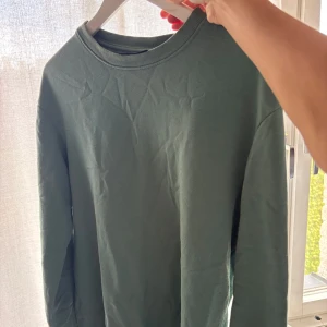 Grön sweatshirt - Säljer en stilren grön crewneck sweatshirt från H&M i relaxed fit. Tröjan har rund halsringning, långa ärmar och är gjord i mjuk bomullsmix. Perfekt för en chill och avslappnad look.