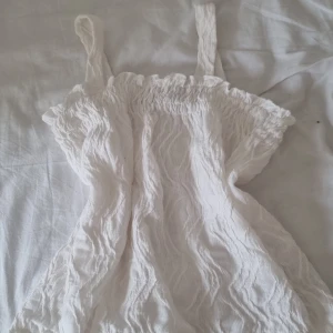 Snygg trendig vit babydoll top - Supersöt vit linnetopp från Kappahl med smock upptill och breda axelband. Toppen har en vågig, strukturerad yta som ger en chill och somrig känsla. Perfekt till shorts eller kjol när det är varmt ute!