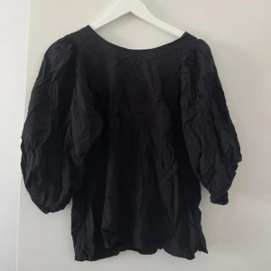 Svart blus med puffärmar - Svart blus med voluminösa puffärmar och snygg snörning i nacken. Tunt, lätt material som ger en luftig känsla. Perfekt för dig som gillar en trendig och avslappnad look med extra volym i ärmarna.