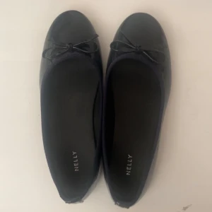 Mörkblå ballerinaskor från Nelly - Säljer ett par jätte söta ballerinaskor från Nelly med en liten rosett framtill. Skorna har en glansig finish och platt sula, vilket ger en stilren och enkel look. Perfekta att matcha med både jeans och klänning. Perfekt till sommaren och skolstarten🤗 ENDAST ANVÄNDA 1 GÅNG 
