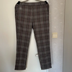 Rutig kostymbyxa från H&M, brun/svart - Snygga kostymbyxor från H&M i storlek 38 med klassiskt rutigt mönster i brunt, svart och vitt. 