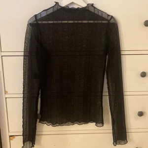 Svart meshblus från Gina Tricot - Säljer en svart transparent meshblus från Gina Tricot i storlek S. Blusen har lång ärm, hög hals med liten volangkant och vågig avslutning vid ärmslut och nederkant. Aldrig använt då jag ej fått tillfälle så är som ny. 🥰