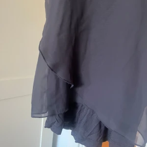 Svart linnetopp från ONLY - Säljer en svart linnetopp från ONLY Love Collection i storlek S. Toppen har ett lager av tunn, transparent polyester med asymmetrisk volangkant och brottarrygg. Perfekt för dig som gillar en luftig och stilren look.