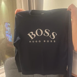 Mörkblå tröja Hugo Boss (PRISET KAN DISKUTERAS VID SNABB AFFÄR) - Snygg mörkblå långärmad tröja från Hugo Boss med stor vit logga framtill. Klassisk passform och rund halsringning, perfekt för dig som gillar stilrena och trendiga plagg med tydlig branding. Dessutom i nyskick och knappt använd.