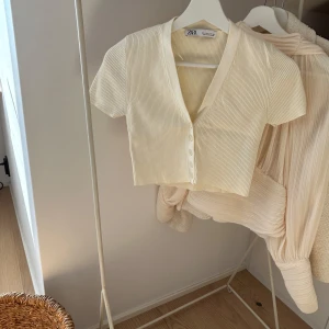 Ribbad croppad topp från Zara - Ljusbeige croppad topp från Zara med korta ärmar och v-ringning. 