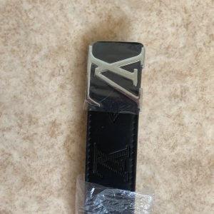 Svart L bälte med silver logga 110cm - Snyggt svart L bälte med silver logga