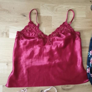 Röd satinlinnetopp Victoria's Secret - Supersnygg röd linnetopp från Victoria's Secret i glansig satin med spetsdetaljer vid urringningen. Tunt axelbandslinne med v-ringad front och romantisk känsla. Perfekt att styla med jeans eller kjol för en trendig look.