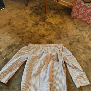 Randig offshoulder skjorta från Zara - Säljer en blåvit randig offshoulder skjorta från Zara Woman. Skjortan har trekvartsärmar och elastisk kant upptill för en snygg passform. Perfekt för dig som gillar en trendig och avslappnad stil.