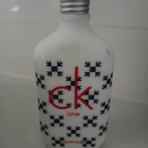 CK One Limited Edition parfym - Unisexparfym från Calvin Klein, CK One Limited Edition. Flaskan är vit med svarta geometriska mönster och röd logotyp. Den har en rundad form och metallfärgad skruvkork. Perfekt för dig som gillar stilren och modern design.
