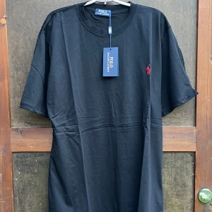 Svart t-shirt från Polo Ralph Lauren - Svart t-shirt från Polo Ralph Lauren med klassisk röd broderad logga på bröstet. Oversized fit, rund halsringning och korta ärmar. Tillverkad i mjuk bomull för en skön känsla. Perfekt basic-plagg med stilren vibe.