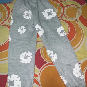 Denim Ters byxor - Grå mjukisbyxor från Denim Ters med vita blommiga tryck över hela byxorna. De har resår och snörning i midjan samt muddar vid bensluten. Perfekta för en chill och avslappnad stil.