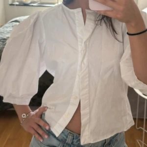 Vit skjorta med puffärm och knappar - Snygg vit skjorta med puffiga trekvartsärmar och knappar framtill. Skjortan har en rak passform och är tillverkad i bomull, perfekt för en trendig och fräsch look. Enkel att styla med jeans eller kjol. lånad bild