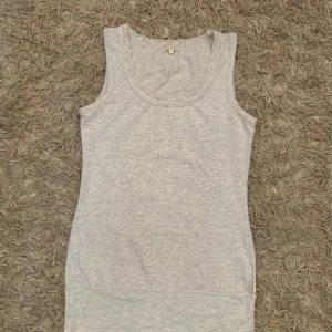 Ljusgrå linnetopp med spets från Bik Bok - Supersöt ljusgrå linnetopp från Bik Bok med spetsdetaljer runt urringningen. Toppen är ärmlös och har en mjuk, stretchig känsla i bomullsmix. Perfekt att styla med jeans eller kjol för en chill look.