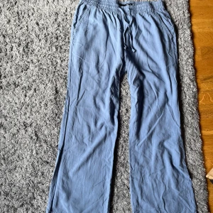 Blå linnebyxor med snörning från 157 - Lätta och sköna blå linnebyxor från 157 med elastisk midja och snörning. Byxorna har raka ben och sidofickor. Materialet är svalt och mjukt, vilket gör dem bra för varmare väder.