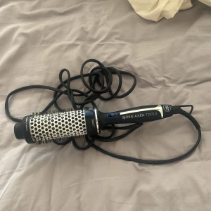 Björn Axén Tools varmluftsborste - En svart och silver varmluftsborste från Björn Axén Tools med rund borste och keramisk yta. Perfekt för att styla och ge volym till håret. Borsten har svarta och vita detaljer samt ett långt sladdfäste för enkel användning.