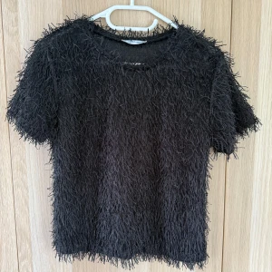 Svart fransig topp från Zara Trafaluc - Cool svart topp från Zara Trafaluc med korta ärmar och massor av fransiga detaljer över hela plagget. Den har en rund halsringning och är tillverkad i ett mjukt, syntetiskt material som ger en unik textur och edgy vibe.