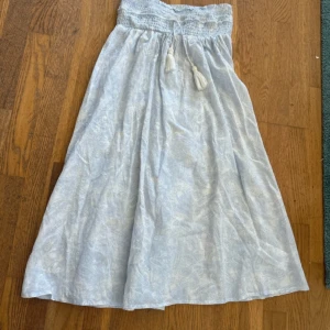 Ljusblå långkjol från Gina Tricot - Supersöt ljusblå långkjol från Gina Tricot med diskret paisleymönster. Kjolen har smock i midjan och dekorativa knytband med tofsar. Perfekt för en chill sommardag eller när du vill ha en luftig och bekväm stil.💗