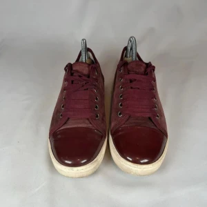 Vinröda sneakers lanvin - Snygga vinröda sneakers med ovandel i mocka och lackad tå. Skorna har snörning och vit sula som ger en cool kontrast. Perfekta för dig som vill ha en stilren men ändå unik look.