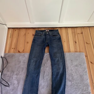 Levi's 501 blå jeans W28 L32 - Klassiska Levi's 501 jeans i blå denim med raka ben och normal passform. Byxorna har fem fickor, knappgylf och ikonisk läderpatch bak i midjan. Perfekta för dig som gillar tidlös stil och vill ha ett par jeans som funkar till allt.