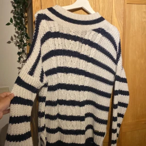 Randig stickad tröja i blått och vitt - Säljer en mysig stickad tröja med breda marinblå och vita ränder. Tröjan har kabelstickat mönster, rund hals och långa ärmar. Perfekt för kyliga dagar när du vill vara både bekväm och snygg.