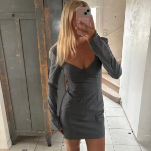 Zara klänning - Snygg grå kortklänning med figurnära passform och markerad byst. Klänningen har långa ärmar med dragkedja vid ärmslut och en stilren, minimalistisk look. Perfekt för dig som gillar en clean och modern stil.