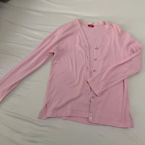 Ljusrosa kofta från Hanin - Supersöt ljusrosa kofta från Hanin i mjuk bomull. Den har v-ringning, långa ärmar och knäppning framtill med små matchande knappar. Perfekt att slänga över en topp för en chill och söt look.