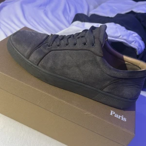 Grå mockasneakers från Louboutin - Snygga grå sneakers från Christian Louboutin i mocka med klassisk röd sula och gråa snören. Skorna har en stilren design med rund tå och platt sula, perfekta för dig som vill ha något exklusivt men ändå casual. Kommer med originalkartong och dustbags.