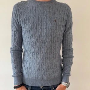 HELT NY KABELSTICKAD MORRIS TRÖJA  - Snygg grå kabelstickad tröja från Morris med rund hals och diskret logga på bröstet. Tröjan är i mjuk 100% merinoull. Perfekt för dig som gillar klassisk och stilren look.