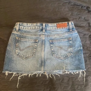 Blå jeanskjol från ONLY med fransig kant - Säljer en blå jeanskjol från ONLY i klassisk denim med fransig, rå nederkant och bakfickor. Kjolen har bälteshällor och en snygg, avslappnad vibe. Perfekt för dig som gillar en cool och trendig stil.