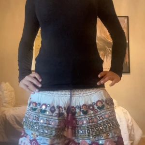 Zara Vit kortkjol med broderi och speglar - Superfin vit kortkjol med broderade blommor i färger som rosa, blått och grönt. Kjolen har små speglar, volanger och en snörning med tofsar i midjan. Denr ifrån Zara.