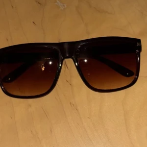 Helt nya bruna solglasögon  - Helt nya Snygga solglasögon med svarta bågar och brunt tonade glas. Klassisk design som passar till många olika stilar. Perfekta för soliga dagar och ger en cool vibe.