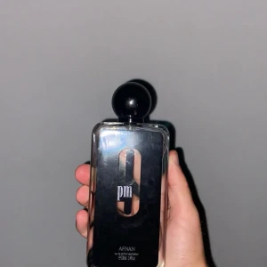 Afnan 9pm Eau de Parfum 100ml - Afnan 9pm är en parfym i en stilren, rektangulär glasflaska med svart etikett och stor svart rund kork. Flaskan rymmer 100 ml och har en modern, minimalistisk design med tydlig logga på framsidan. INGEN LÅDA!!!
