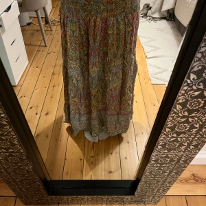 Mönstrad långkjol i boho-stil - Långkjol med färgglatt blommigt mönster i grönt, rött och gult. Smockad midja för skön passform och flowy kjol. Perfekt för sommarens varma dagar och festivaler. Tunt, luftigt material som känns lätt mot huden.